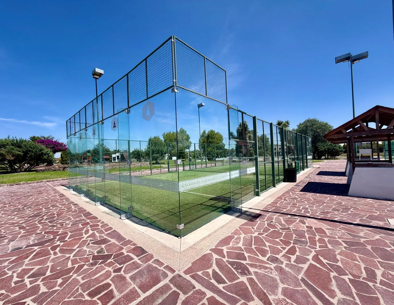 Cancha de pádel de Alquerías con cerramiento de cristal y áreas verdes alrededor.